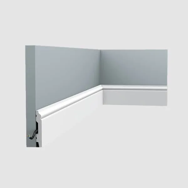 Orac SX165 skirting installed in a room corner on gray walls, shown in white against the floor-level wall base