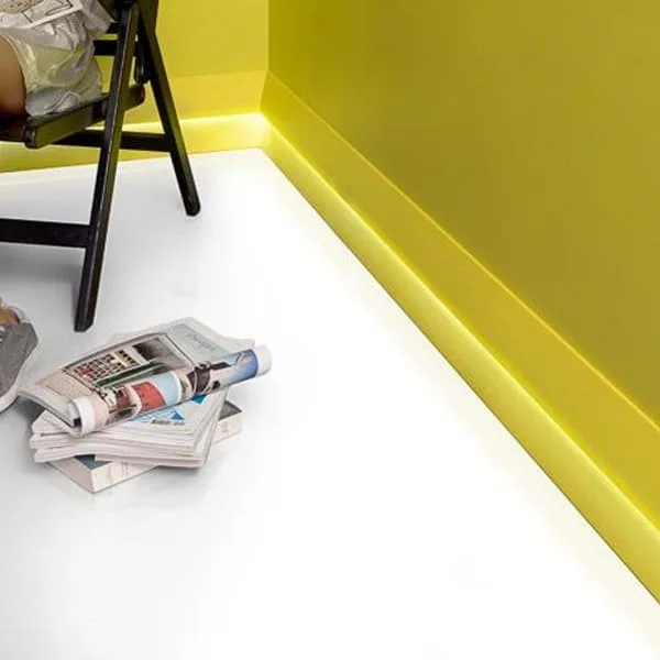 Orac SX179 skirting on yellow wall with white floor, black chair and folded newspapers